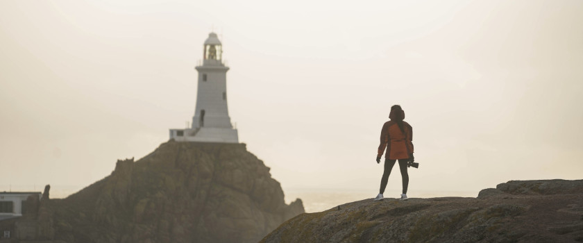 A traveler looks at La Corbiere Lighthouse in the distance