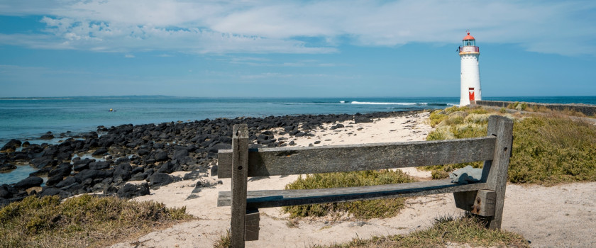 Bench on the beach overlooking a lighthouse.