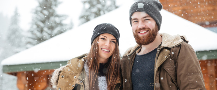 Couple standing outside a log cabin in winter.