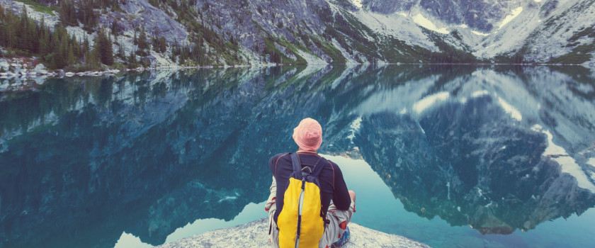 Person sits on a rock overlooking an alpine lake.