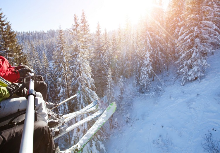 family sitting in ski lift skis danging over winter scene